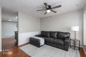Living area with dark wood-type flooring, a ceiling fan, and wainscoting