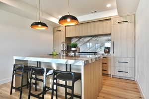 Kitchen featuring light wood finish cabinetry, pendant lighting, modern cabinets, light stone countertops, and a kitchen breakfast bar