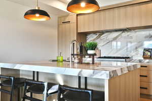 Kitchen with light wood finish cabinets, modern cabinets, light stone counters, decorative light fixtures, and a kitchen breakfast bar