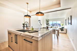 Kitchen with modern cabinets, a center island with sink, a raised ceiling, light stone counters, and open floor plan