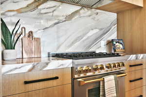 Kitchen featuring high end range, light wood finish cabinets, modern cabinets, and light stone counters