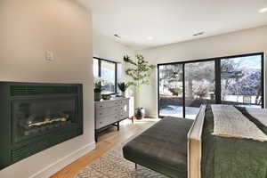 Bedroom featuring a glass covered fireplace, light wood finished floors, access to exterior, and recessed lighting