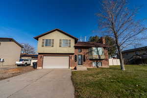 Split level home featuring brick siding, concrete driveway, a garage, and a chimney