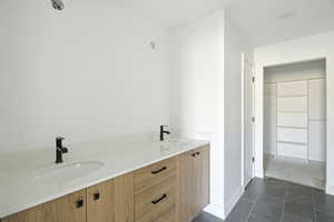 Full bath with double vanity, a spacious closet, and dark tile patterned floors