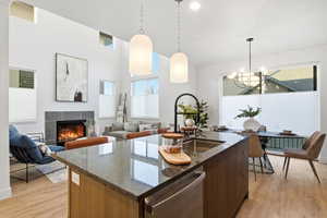 Kitchen featuring dark stone countertops, a center island with sink, pendant lighting, dishwasher, and light wood finished floors
