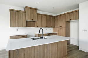Kitchen with brown cabinets, light stone counters, a center island with sink, and light wood finished floors