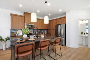 Kitchen with a breakfast bar, brown cabinets, dark stone counters, decorative light fixtures, and stainless steel appliances