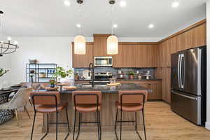 Kitchen featuring stainless steel appliances, dark stone countertops, hanging light fixtures, an island with sink, and a kitchen breakfast bar