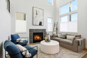 Living area featuring a tile fireplace, healthy amount of natural light, wood finished floors, and a high ceiling