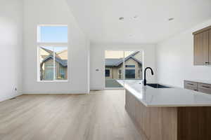 Kitchen featuring light wood-style flooring, plenty of natural light, light stone counters, an island with sink, and a high ceiling