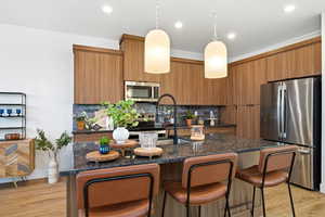 Kitchen featuring stainless steel appliances, a kitchen bar, decorative light fixtures, dark stone counters, and recessed lighting