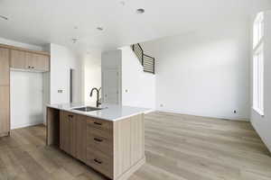 Kitchen featuring modern cabinets, light wood-style floors, light stone countertops, a center island with sink, and brown cabinetry