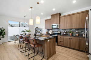 Kitchen featuring dark stone countertops, a kitchen island with sink, modern cabinets, stainless steel appliances, and recessed lighting