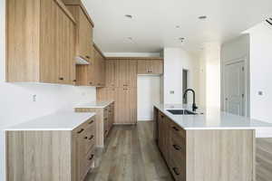 Kitchen featuring light stone countertops, light wood finished floors, a center island with sink, modern cabinets, and brown cabinets
