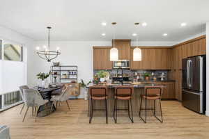 Kitchen with appliances with stainless steel finishes, brown cabinetry, decorative backsplash, a kitchen bar, and decorative light fixtures