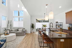 Kitchen with dark stone countertops, pendant lighting, brown cabinetry, a kitchen breakfast bar, and light wood-type flooring