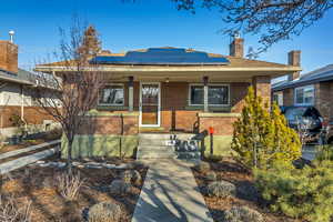 View of front of property with a porch, brick siding, roof mounted solar panels, and a chimney