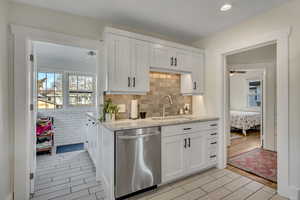 Kitchen featuring white cabinets, stainless steel dishwasher, light stone countertops, and wood tiled floors