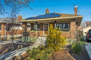 Ranch-style home with brick siding, covered porch, a chimney, and roof mounted solar panels