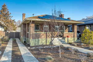 Bungalow-style house with a chimney, solar panels, brick siding, and a porch
