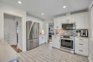 Kitchen with appliances with stainless steel finishes, white cabinets, backsplash, light stone countertops, and recessed lighting