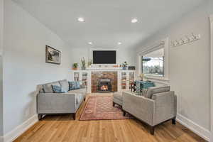 Living room featuring a brick fireplace, light wood-style floors, and recessed lighting