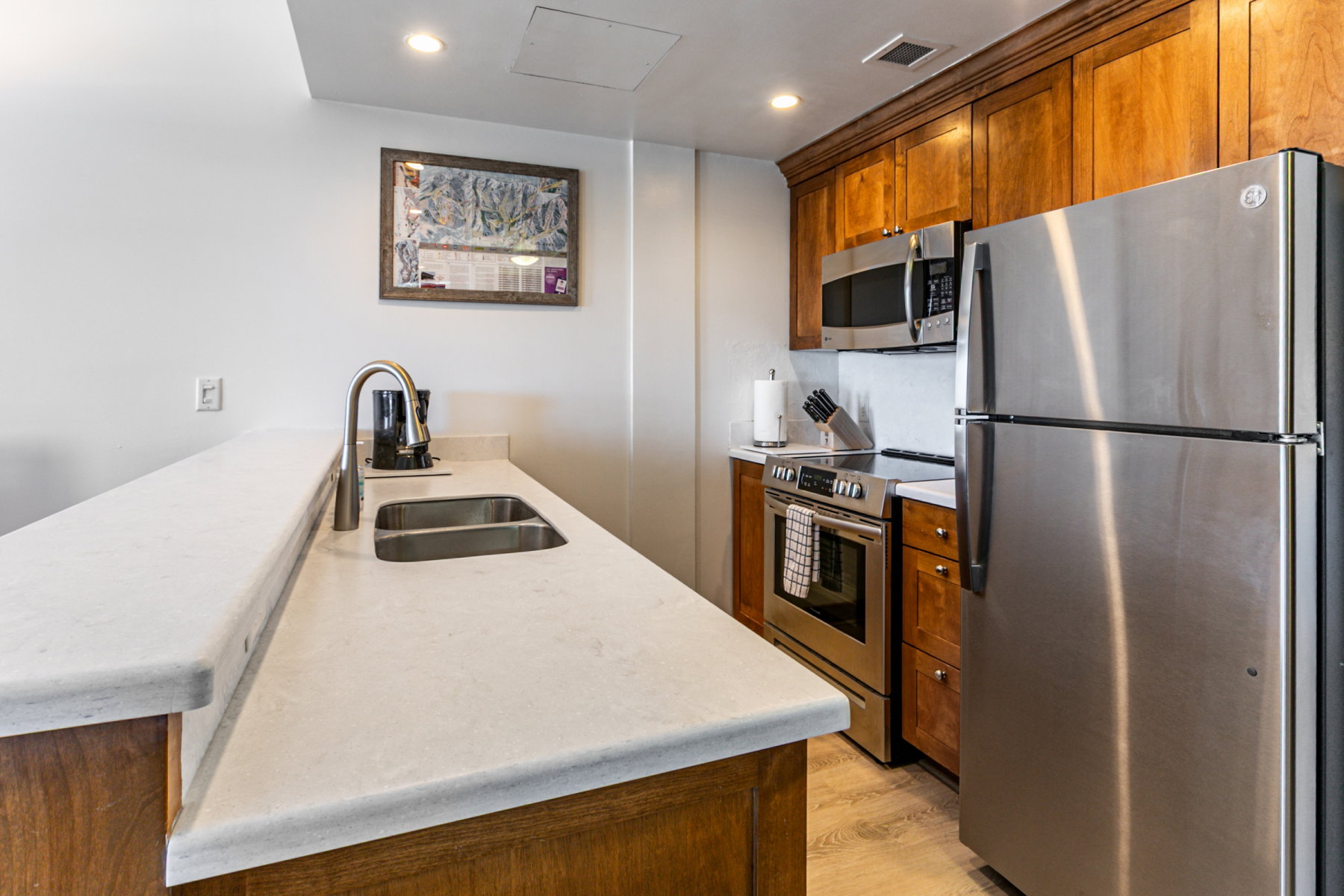 Kitchen featuring stainless steel appliances, a peninsula, brown cabinets, light wood-style flooring, and light stone countertops