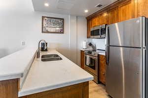 Kitchen featuring stainless steel appliances, a peninsula, brown cabinets, light wood-style flooring, and light stone countertops
