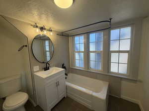 Bathroom with a textured ceiling, vanity,  shower combination, dark tile patterned flooring, and tile walls