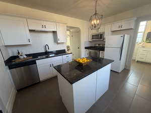 Kitchen featuring appliances with stainless steel finishes, white cabinets, hanging light fixtures, dark stone countertops, and a textured ceiling