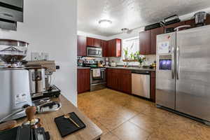 Kitchen featuring stainless steel appliances, a textured ceiling, light tile patterned floors, and light countertops