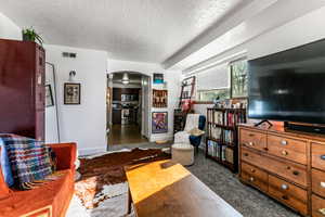 Living area featuring arched walkways, a textured ceiling, and dark carpet