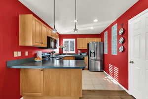 Kitchen with black appliances, dark countertops, hanging light fixtures, a peninsula, and recessed lighting