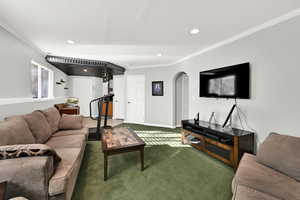 Carpeted living room with ornamental molding, arched walkways, and recessed lighting