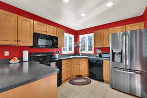 Kitchen with black appliances, dark countertops, a textured ceiling, recessed lighting, and light tile patterned floors
