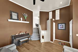 Entrance foyer featuring light wood finished floors, ornamental molding, ceiling fan, stairs, and a towering ceiling