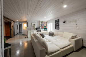 Living area featuring a barn door, wood walls, recessed lighting, wooden ceiling, and finished concrete flooring
