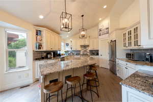 Kitchen with decorative backsplash, a breakfast bar, vaulted ceiling, hanging light fixtures, and light stone countertops