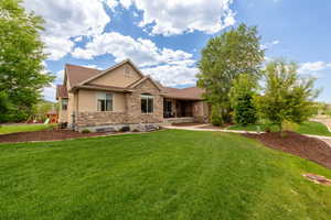 View of front of home with stone siding, a front yard, stucco siding, and a playground