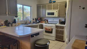 Kitchen with a peninsula, white appliances, light countertops, and a kitchen breakfast bar
