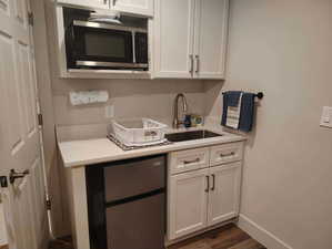 Kitchen featuring stainless steel appliances, white cabinets, dark wood-type flooring, and light stone counters