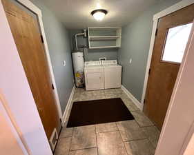 Laundry room featuring a textured ceiling, light tile patterned floors, water heater, and washer and clothes dryer