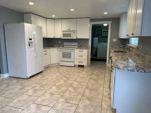 Kitchen with white appliances, light stone counters, white cabinets, washer / clothes dryer, and recessed lighting