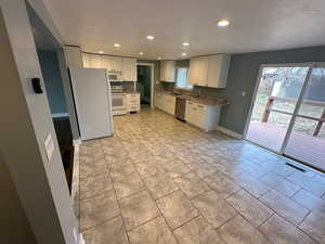 Kitchen featuring white appliances, white cabinets, recessed lighting, and light stone countertops