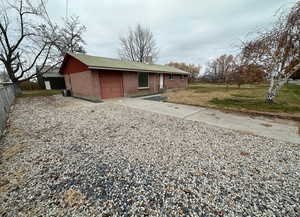 Rear view of house featuring gravel driveway, an attached garage, a shingled roof, brick siding, and a yard