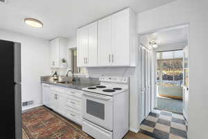 Kitchen with white appliances, white cabinetry, dark flooring, and healthy amount of natural light