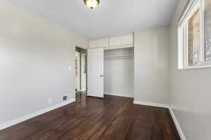 Unfurnished bedroom featuring a closet and dark wood-style floors