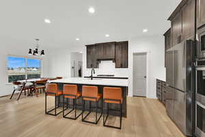 Kitchen featuring appliances with stainless steel finishes, decorative light fixtures, a kitchen breakfast bar, dark brown cabinetry, and recessed lighting