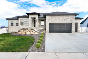 Prairie-style house featuring stone siding, driveway, an attached garage, and a gate