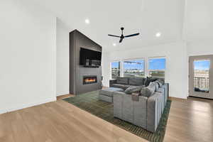 Living room with light wood-type flooring, a fireplace, recessed lighting, a ceiling fan, and high vaulted ceiling